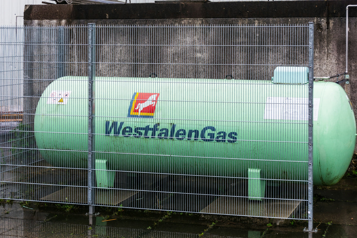 A large green westfalengas storage tank behind a fence