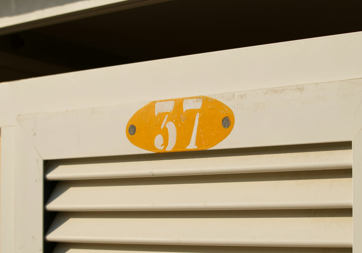 A yellow oval plaque with the number 57 on a white louvered door